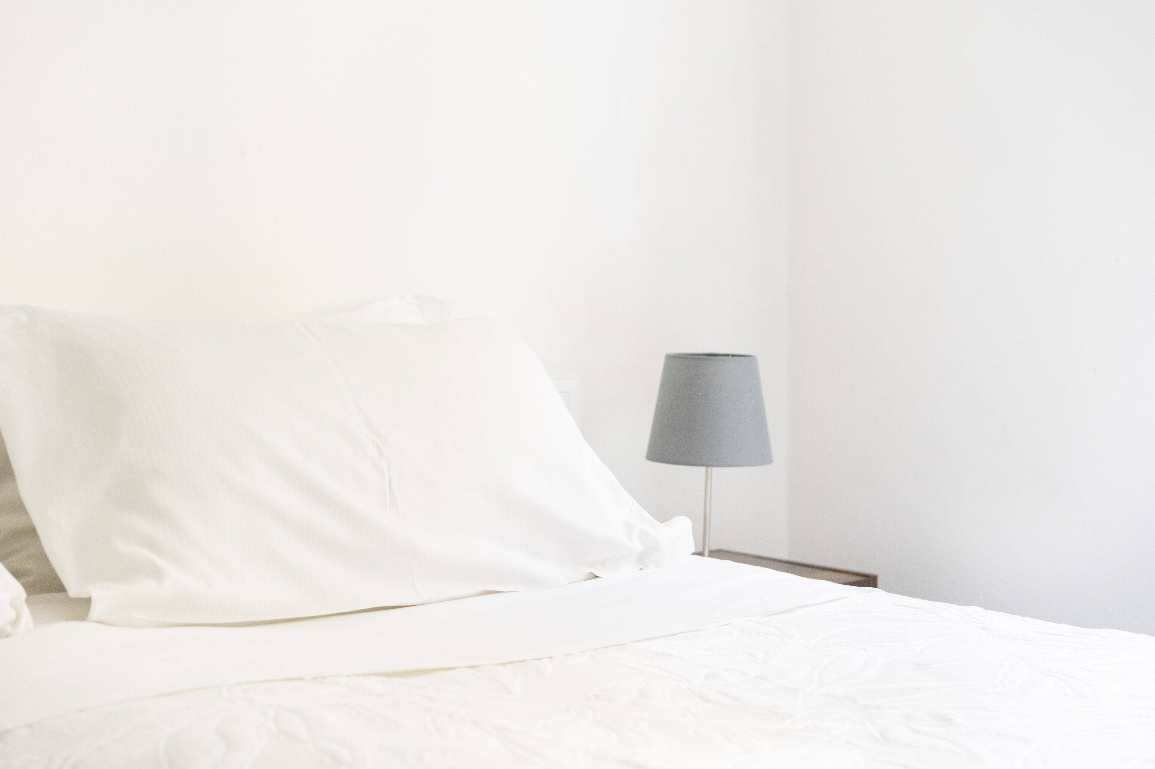 Un lit bien fait, avec du linge de lit blanc et une lampe de chevet grise.