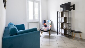 En stue med en blå sofa, en farverig lænestol, et sort tv-møbel og et lille sofabord.