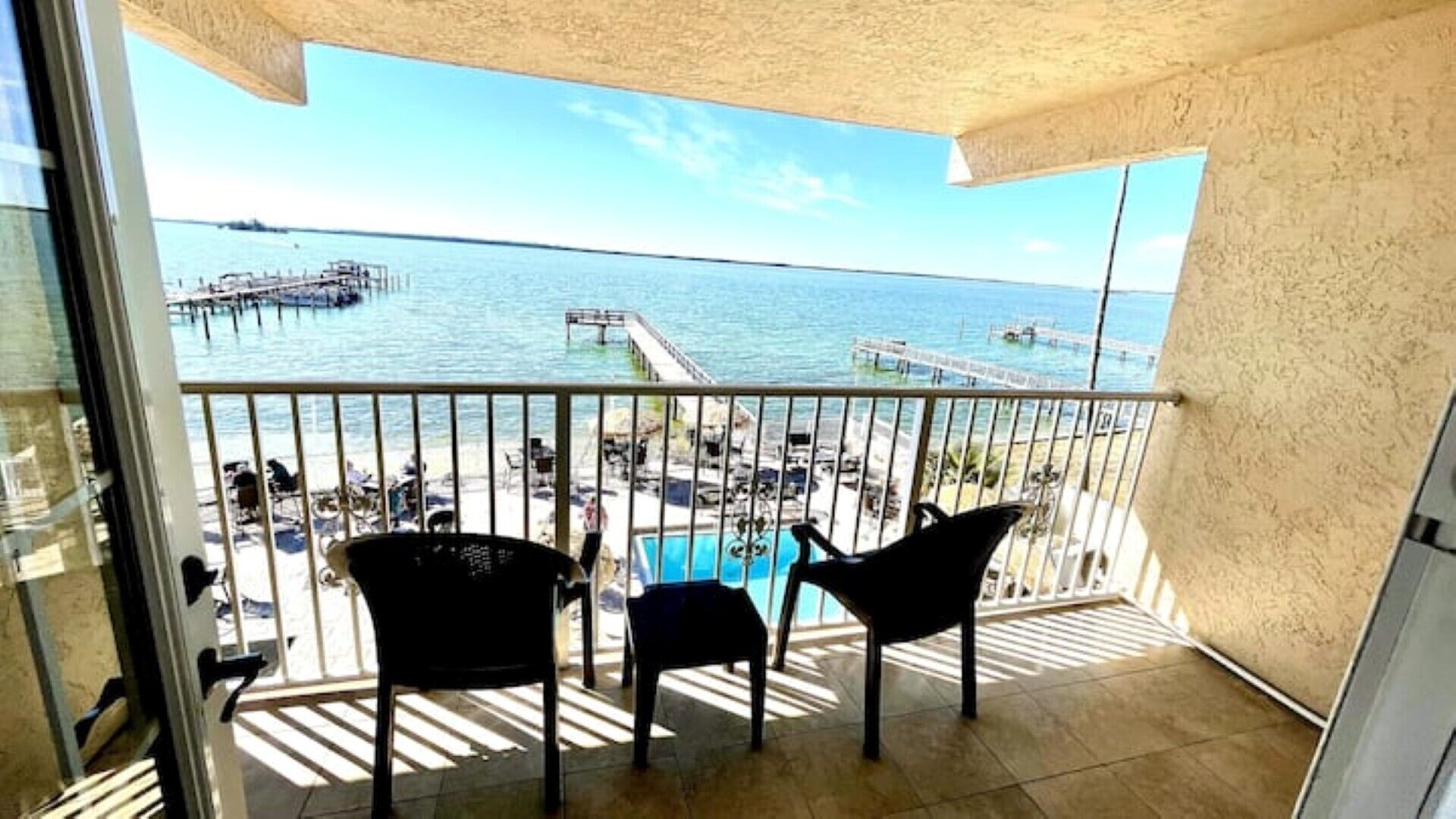 A balcony with a view of a beach and a pier. There are two chairs and a small pool.