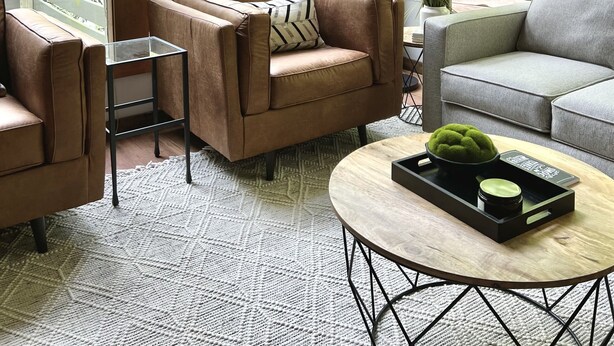 Ein geräumiges Wohnzimmer mit großen Fenstern, einem braunen Ledersofa, einem grauen Sofa und einem runden Couchtisch mit Tablett.