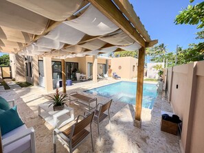 A poolside area with a covered seating area, a pool, and a view of the surrounding landscape.