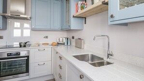 A modern kitchen with white cabinets, a stainless steel oven, a double sink, and a toaster. - Mermaid House (Weymouth)