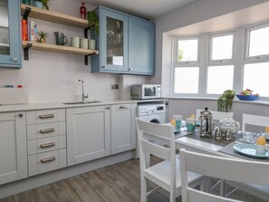Uma cozinha moderna com armários brancos, micro-ondas embutido e um espaço de refeições com uma mesa posta para dois.