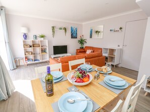 Uma sala de estar moderna com uma mesa de jantar posta para uma refeição, um sofá, uma TV e uma estante de livros.