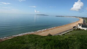 A coastal view with a sandy beach, a clear sky, and a distant landmass. - Mermaid House (Weymouth)