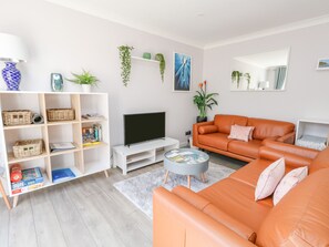 Uma sala de estar moderna com um móvel branco para entretenimento, um sofá grande cor de laranja e uma TV de tela plana.