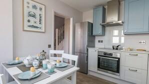 A modern kitchen with white cabinets, a built-in oven, and a dining area with a table set for two. - Mermaid House (Weymouth)