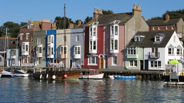 A waterfront with colorful buildings and boats docked along the shore. - Mermaid House (Weymouth)