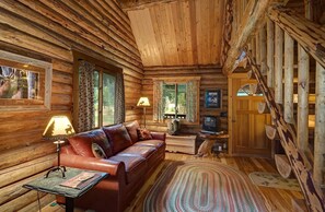 A log cabin interior with a leather sofa, a television, and a fireplace.