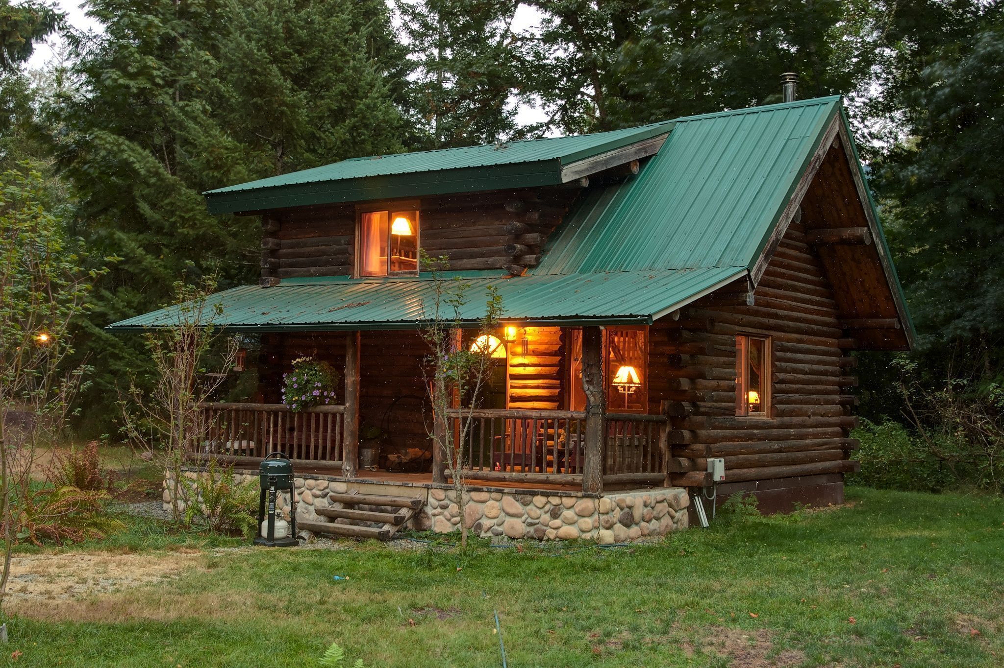 A log cabin with a porch, two windows with lights, and a stone foundation.