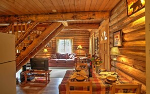 A log cabin interior with a staircase, a living room with a sofa, a dining table set, and a television.