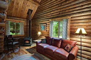 A log cabin interior with a leather sofa, a fireplace, and a large window.