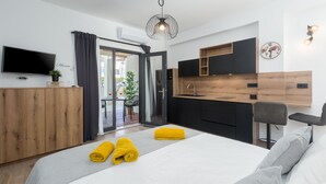 Ein modernes Hotelzimmer mit Bett, Fernseher, Küchenzeile und Balkon.