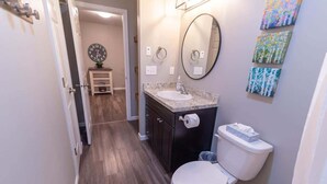 A bathroom with a white toilet, a sink, and a mirror. There are three framed artworks on the wall. - Quiet & Private! 2BD w/ Laundry and Full Kitchen (Meadow Lakes)