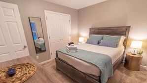 A bedroom with a bed, bedside tables, a mirror, and a door. - Quiet & Private! 2BD w/ Laundry and Full Kitchen (Meadow Lakes)