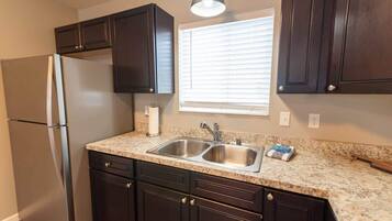 A kitchen with dark cabinets, a stainless steel refrigerator, a double sink, and a window with blinds.