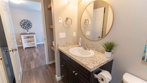 A bathroom with a sink, mirror, toilet, and a clock on the wall. - 2BR Private Suite w/ Full Kitchen & Laundry! (Meadow Lakes)