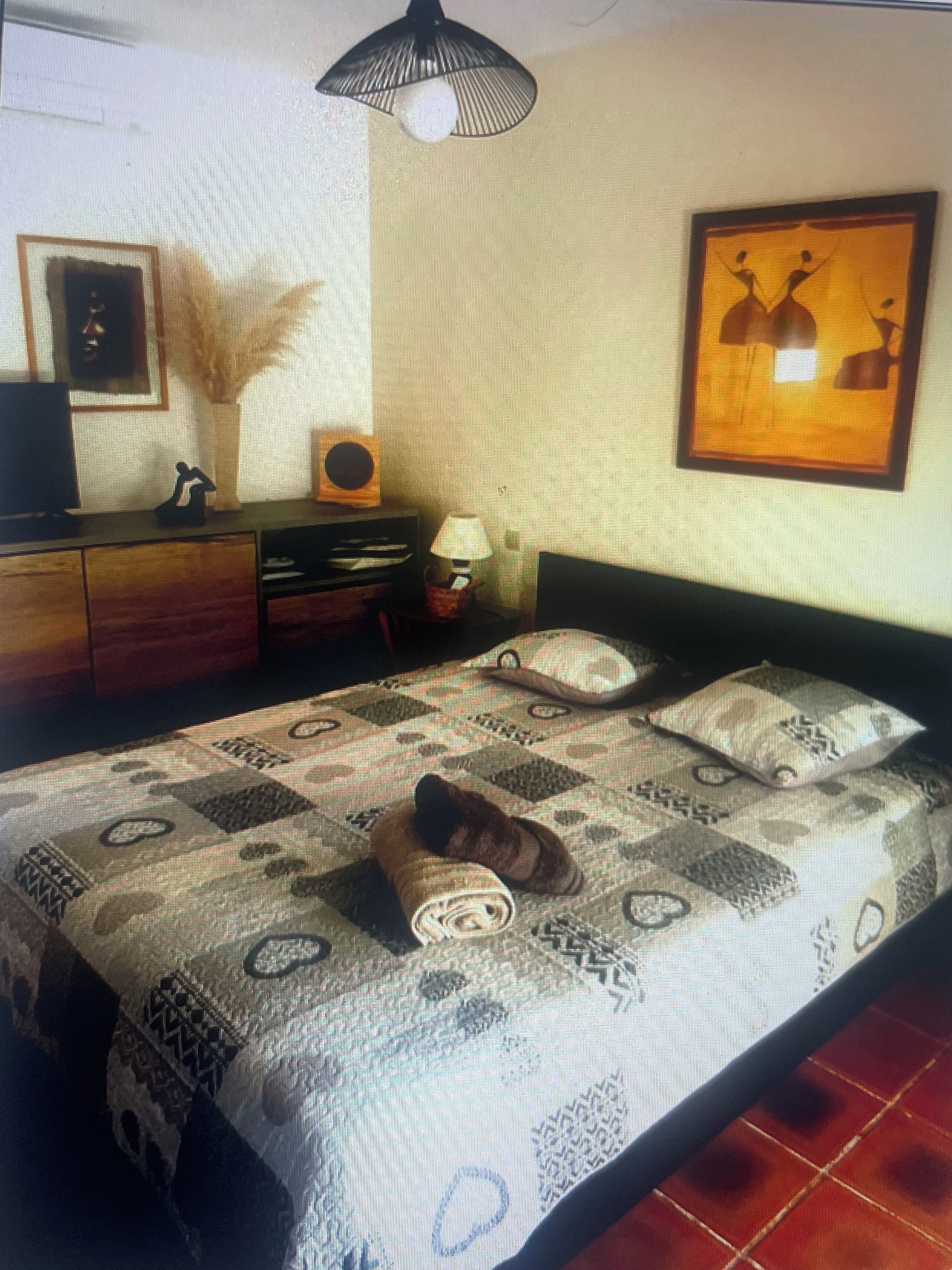 Une chambre à coucher avec un lit, un bureau, une chaise, une lampe et un tableau accroché au mur.