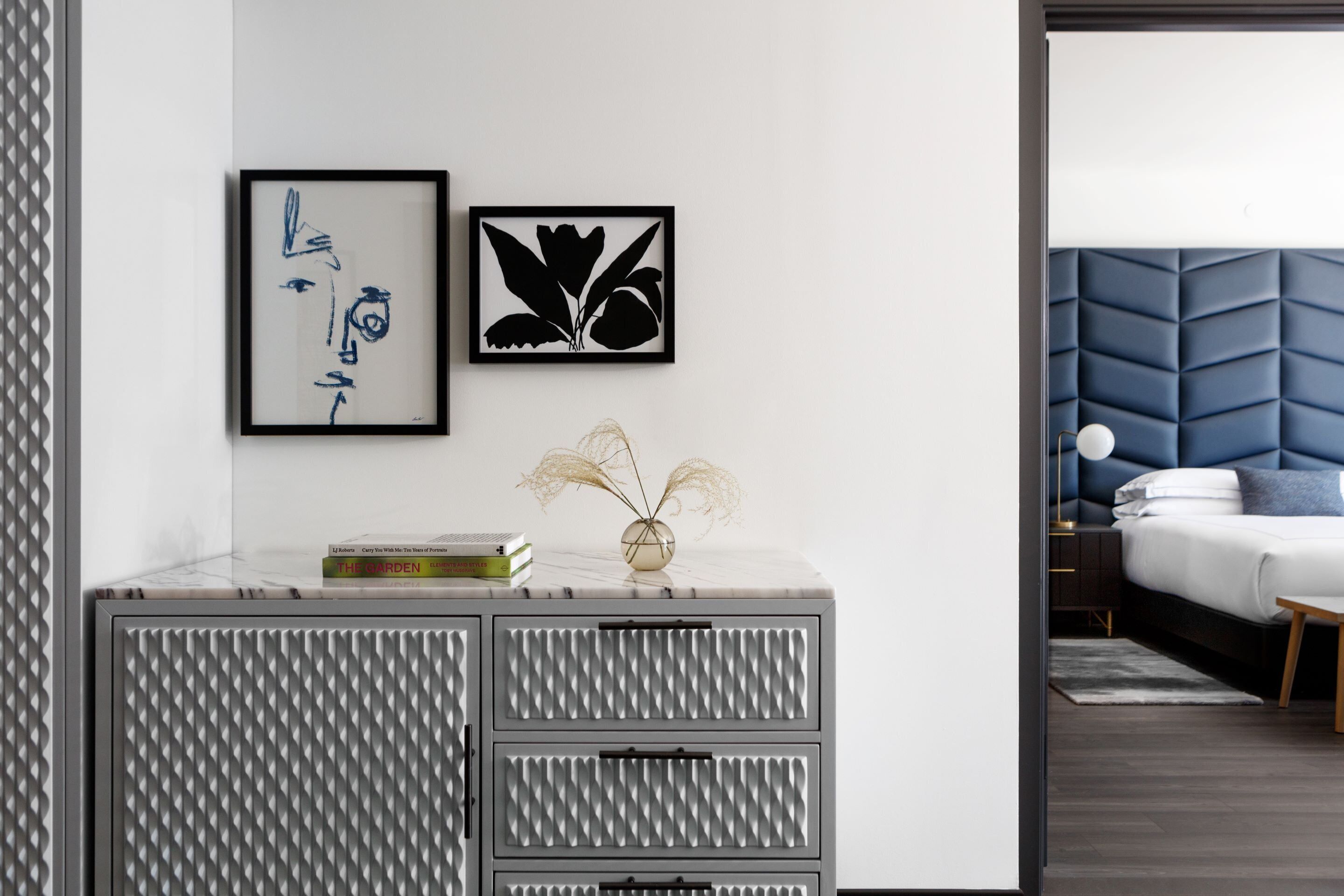 A modern bedroom with a bed, a bedside table with books, and a wall-mounted artwork.