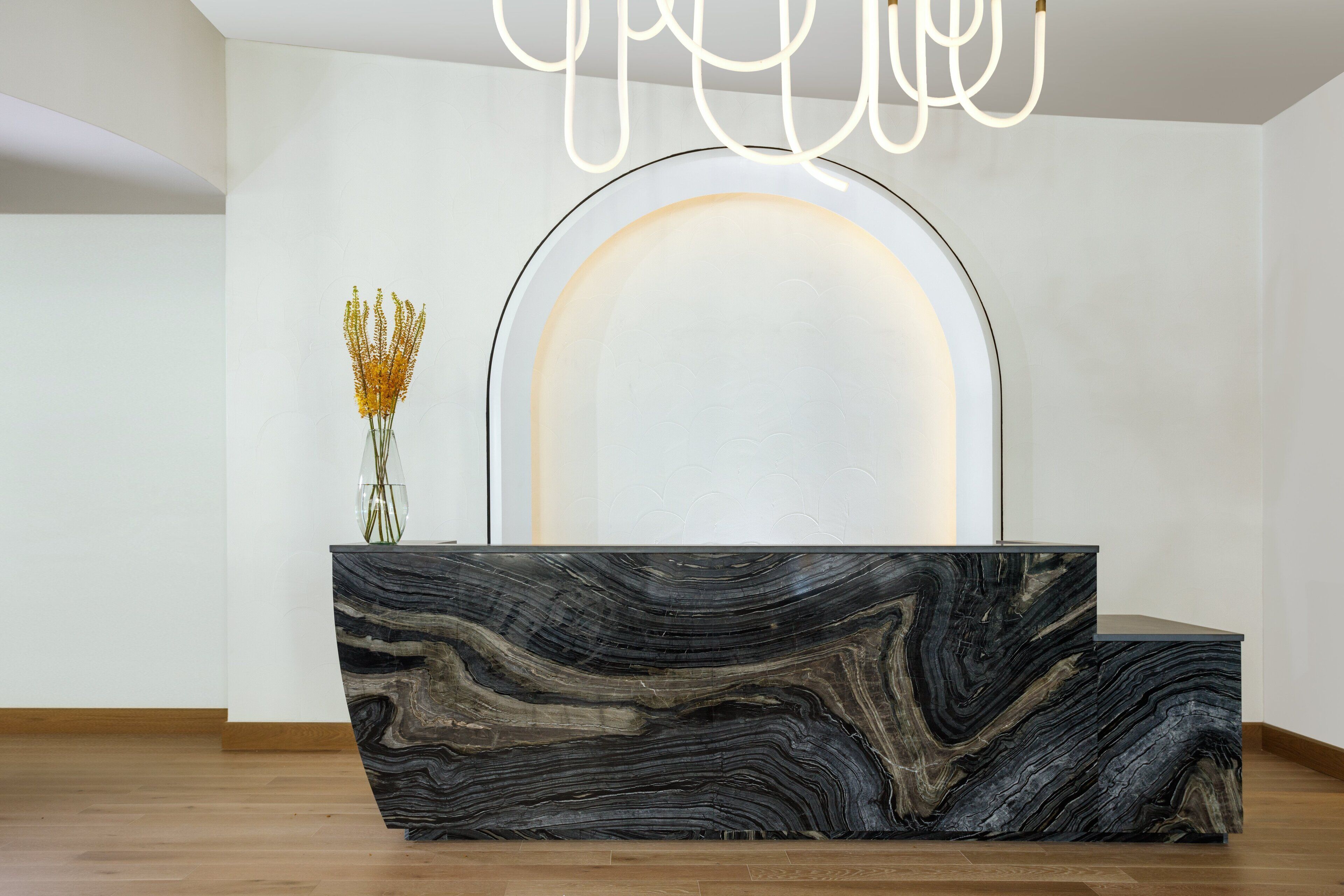 A reception desk with a marble top and a modern light fixture above it.