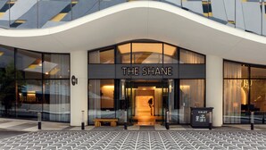 A modern hotel entrance with a curved facade, large glass windows, and a sign reading "THE SHANE".