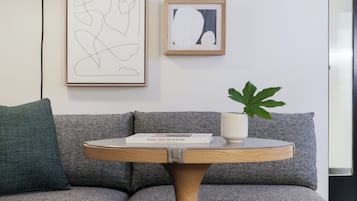 Un salon moderne avec un canapé gris, une table basse ronde en bois et deux œuvres d’art abstraites encadrées accrochées au mur.