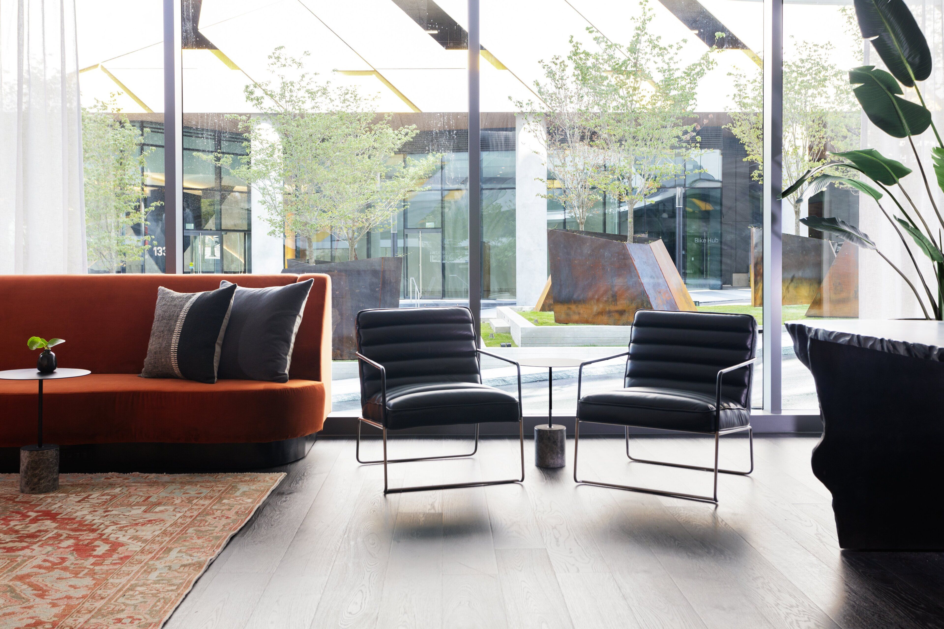 A modern living room with a sofa, two armchairs, a coffee table, and a large window offering a view of a building and greenery outside.