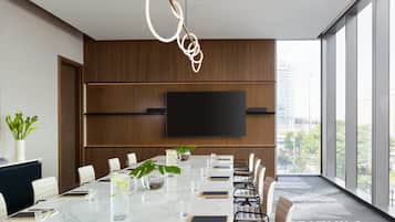 Una sala de conferencias moderna con una mesa grande, sillas, un televisor y vistas a la ciudad.