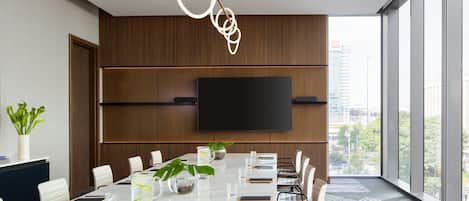 A modern conference room with a large table, chairs, a TV, and a city view.