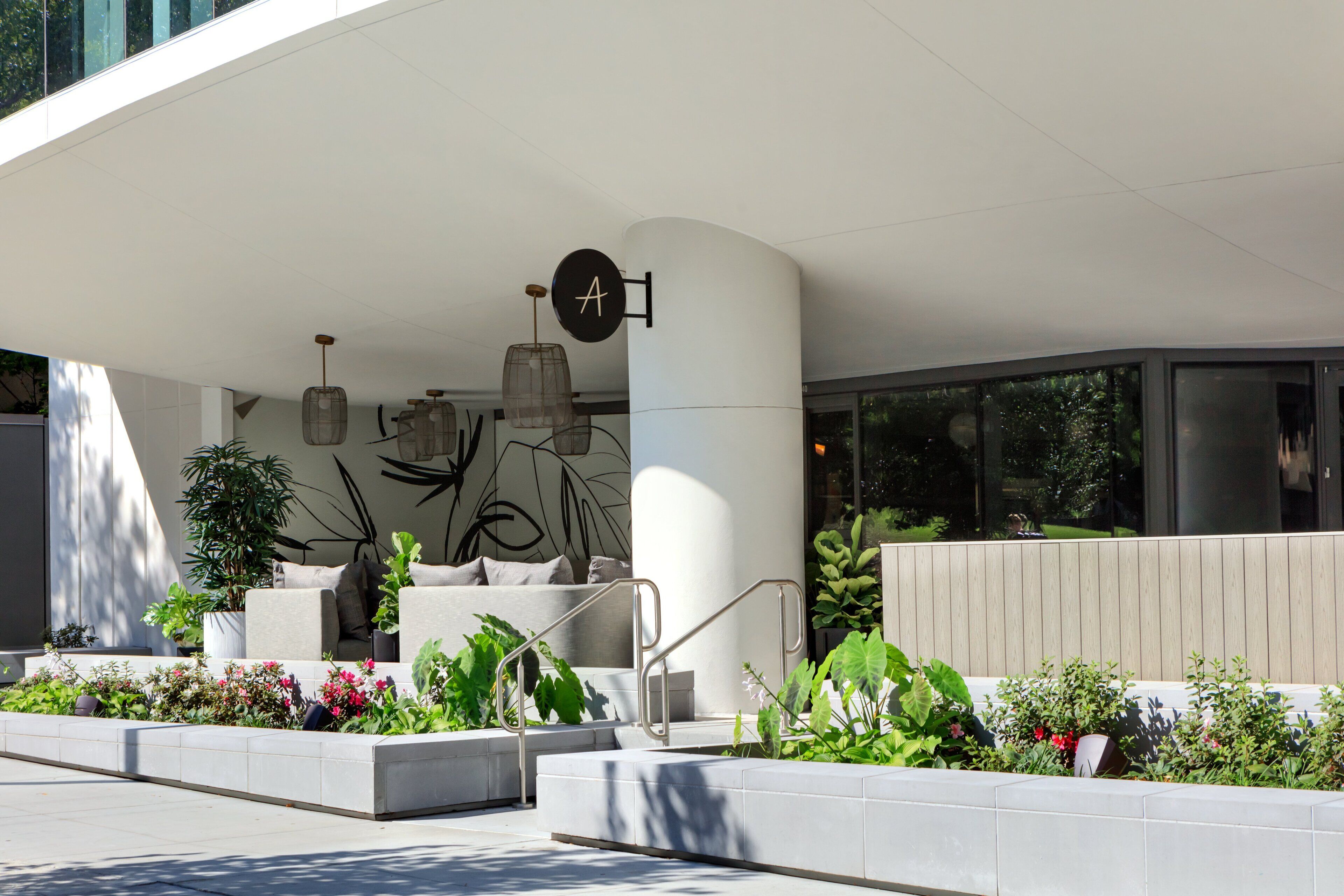A modern hotel entrance with a curved white facade, outdoor seating area with cushions, and a sign with the letter 'A'.