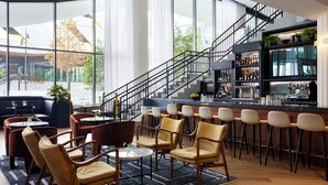 A modern bar area with a curved staircase, seating with cushioned chairs, and a bar stocked with bottles.
