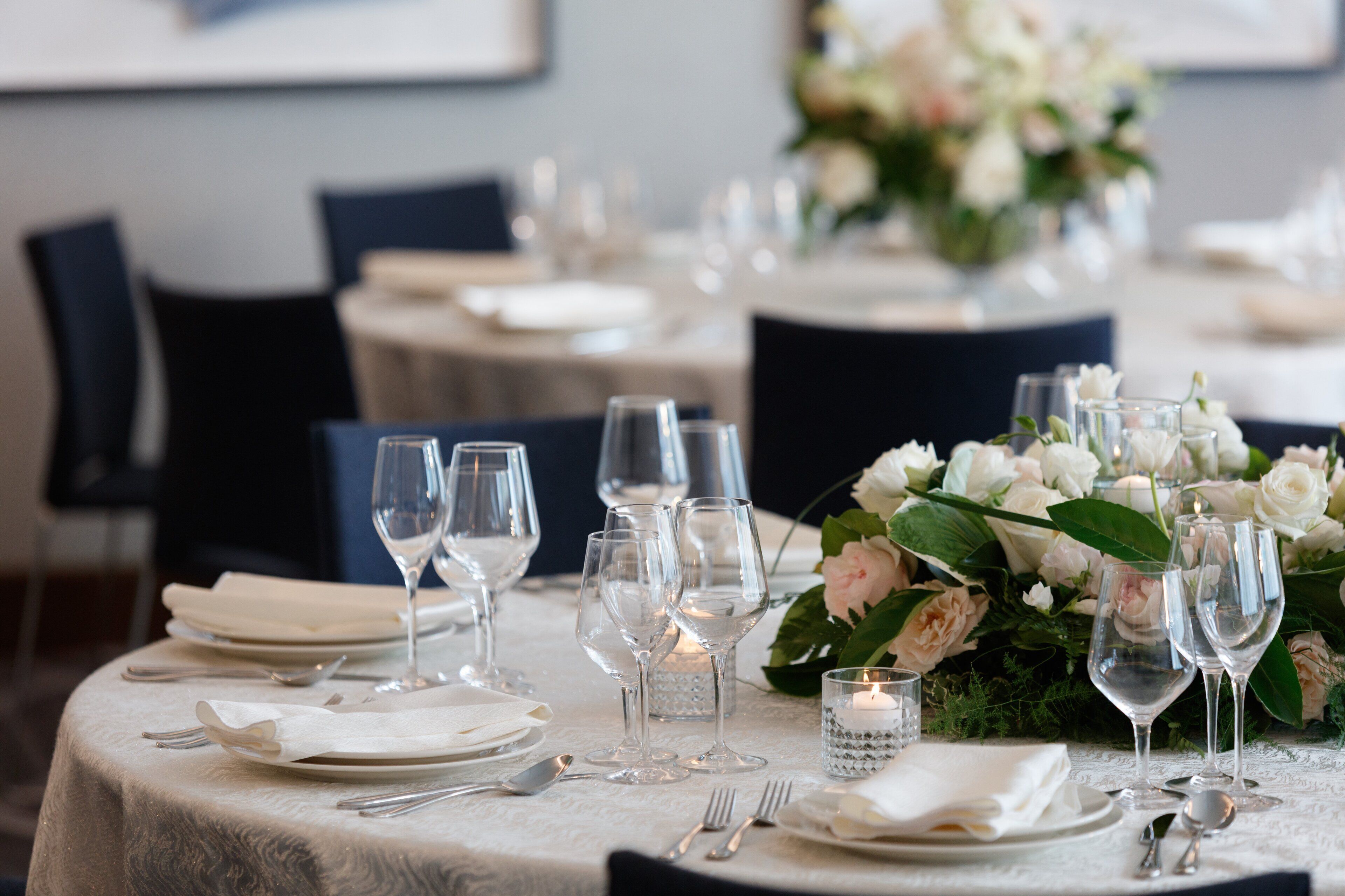 A dining table set with white tablecloth, silverware, and clear wine glasses, surrounded by white flowers and candles.