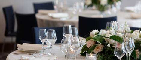 A dining table set with white tablecloth, silverware, and clear wine glasses, surrounded by white flowers and candles.