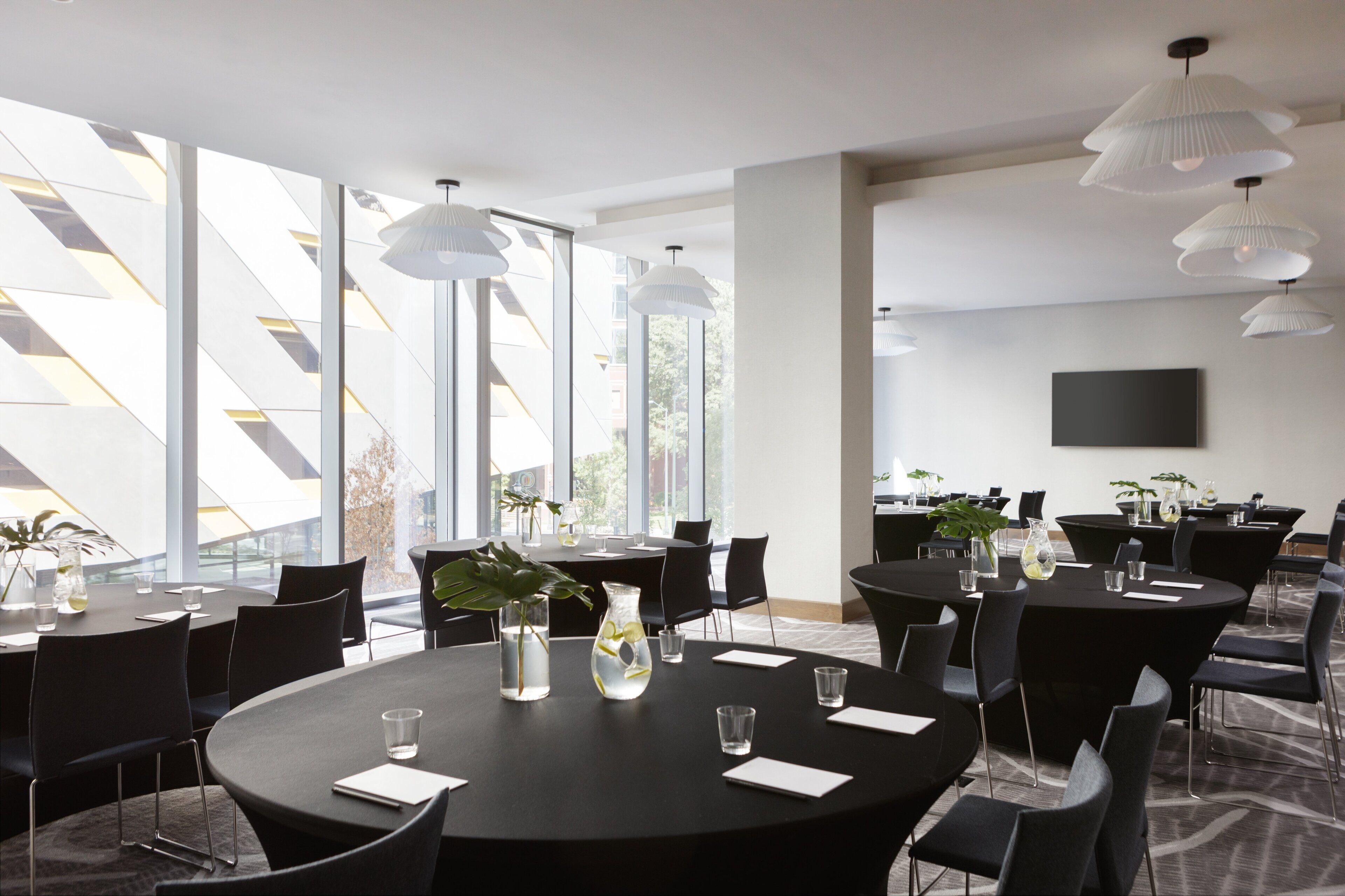 A modern conference room with round tables, black chairs, and white pendant lights.
