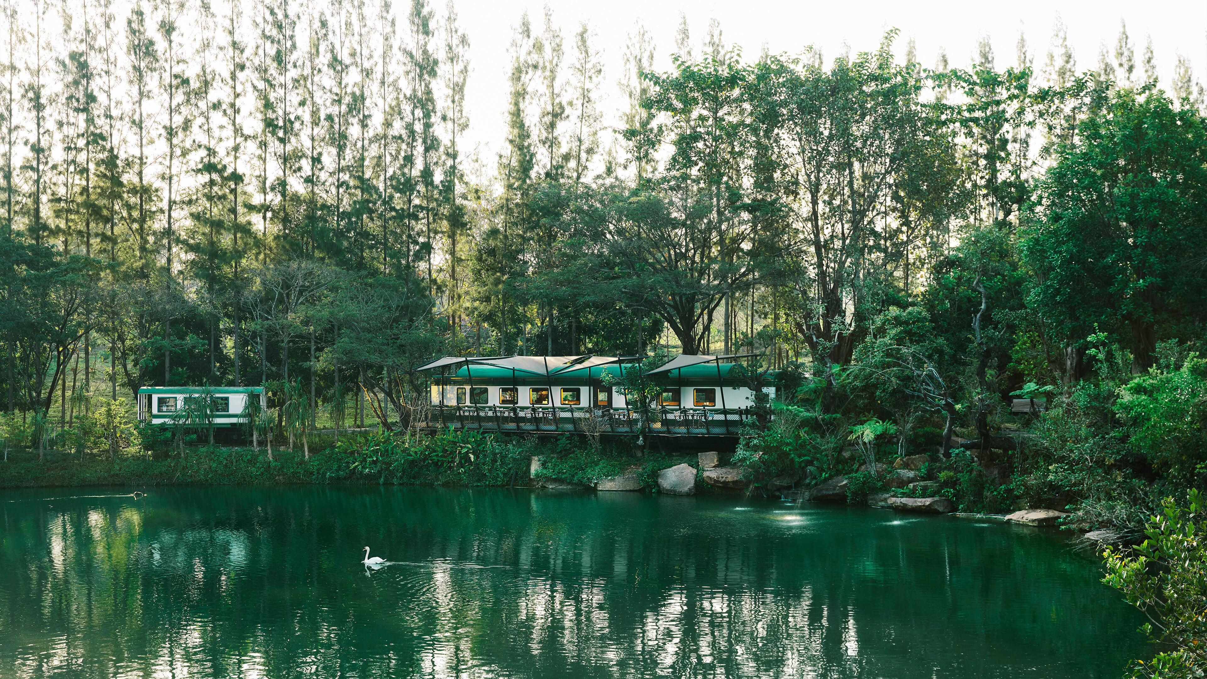 Una hilera de cabañas, con un río al frente y un bosque al fondo.