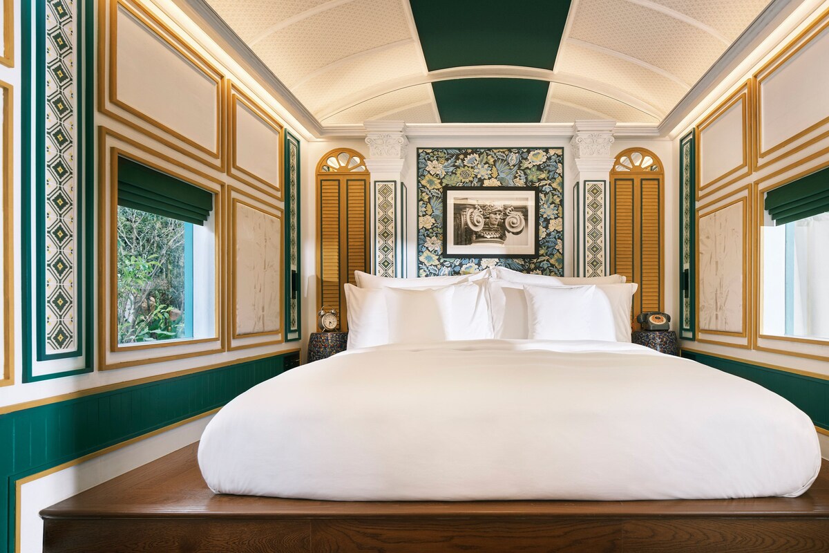 A large bed with white linens in a room with green and gold trim, a clock, and a framed picture on the wall.