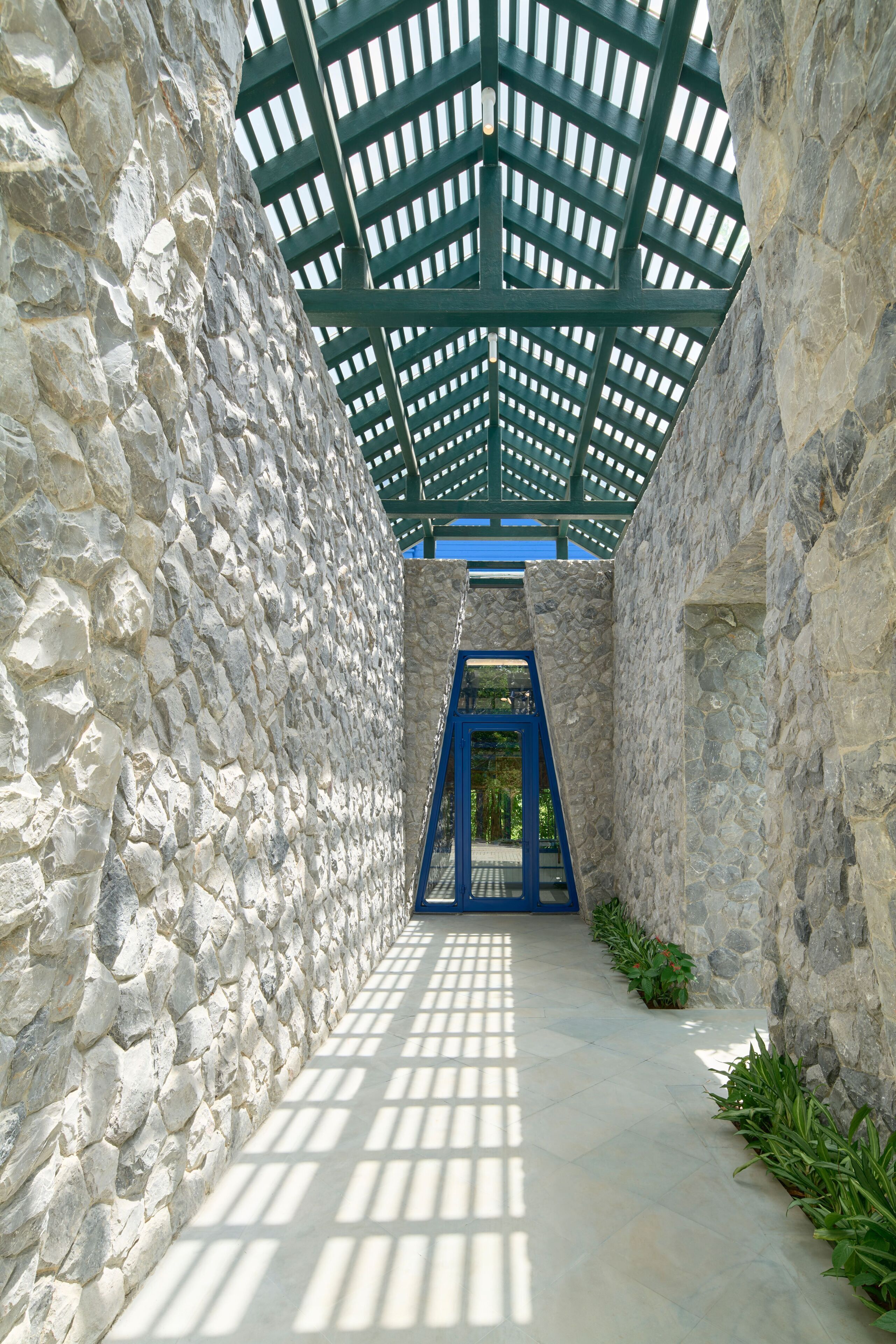 A stone-walled corridor with a blue gate and a green roof structure.