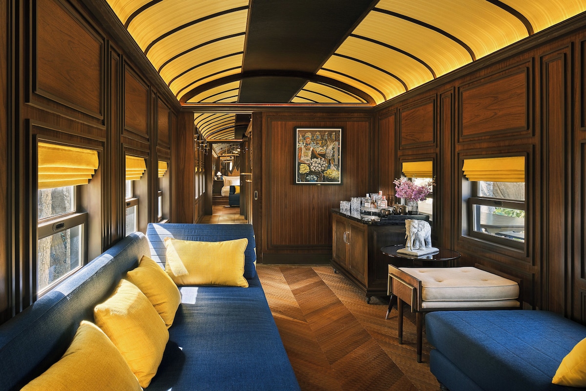 A train car interior with a blue sofa set, wooden paneling, and a curved ceiling.