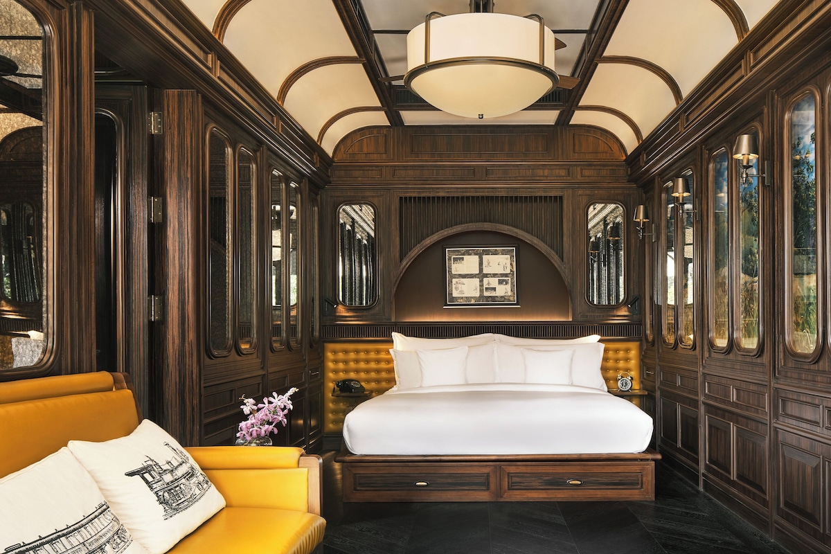 A room with a large bed, a yellow sofa, and a chandelier.