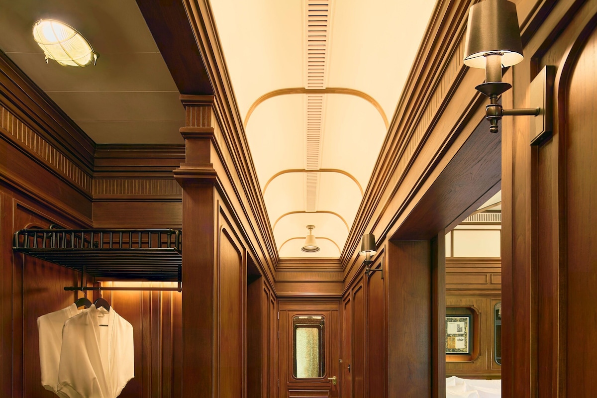 A hotel corridor with wooden paneling, a bench, a coat rack, and a bed with a white bedspread.