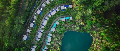Vista aérea de un complejo turístico con varias edificaciones dispuestas en forma curva, un cuerpo de agua central y exuberante vegetación que lo rodea.
