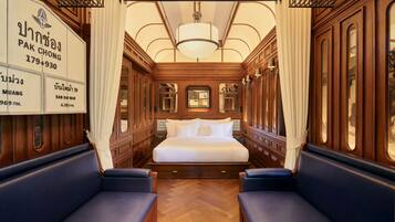 A luxurious train compartment with a large bed, two blue upholstered seats, wooden paneling, and a chandelier.