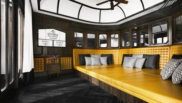 A train car interior with a yellow upholstered bench, a small table with a vase, and a wall-mounted information board.