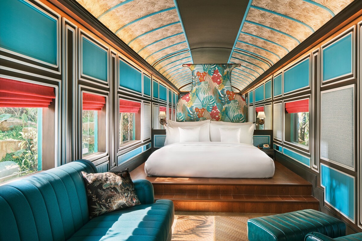 A luxurious train bedroom with a large bed, a sofa, and a view of the outdoors through the windows.