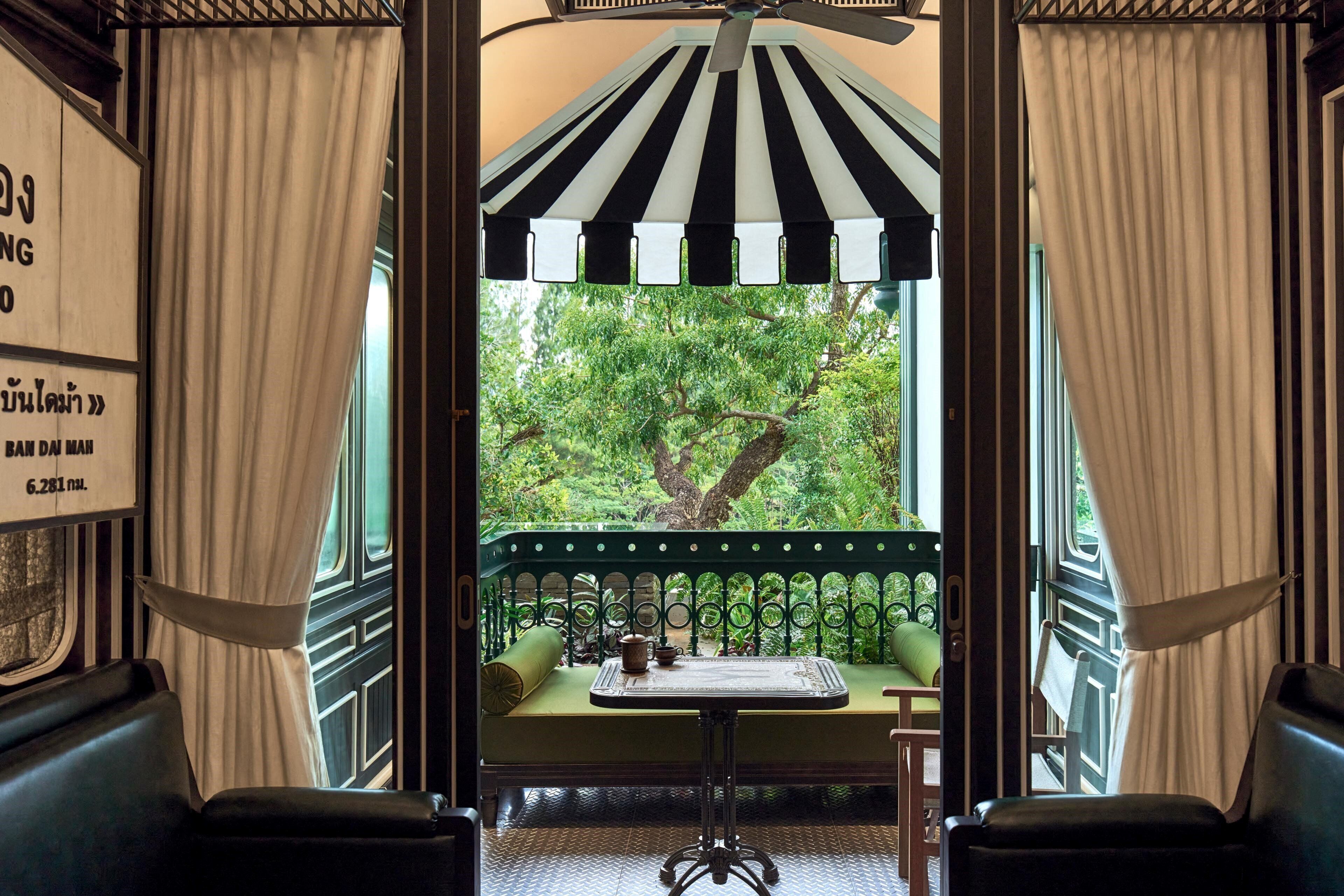 A room with a view of trees through a window, a small table with a cup, and a bench.
