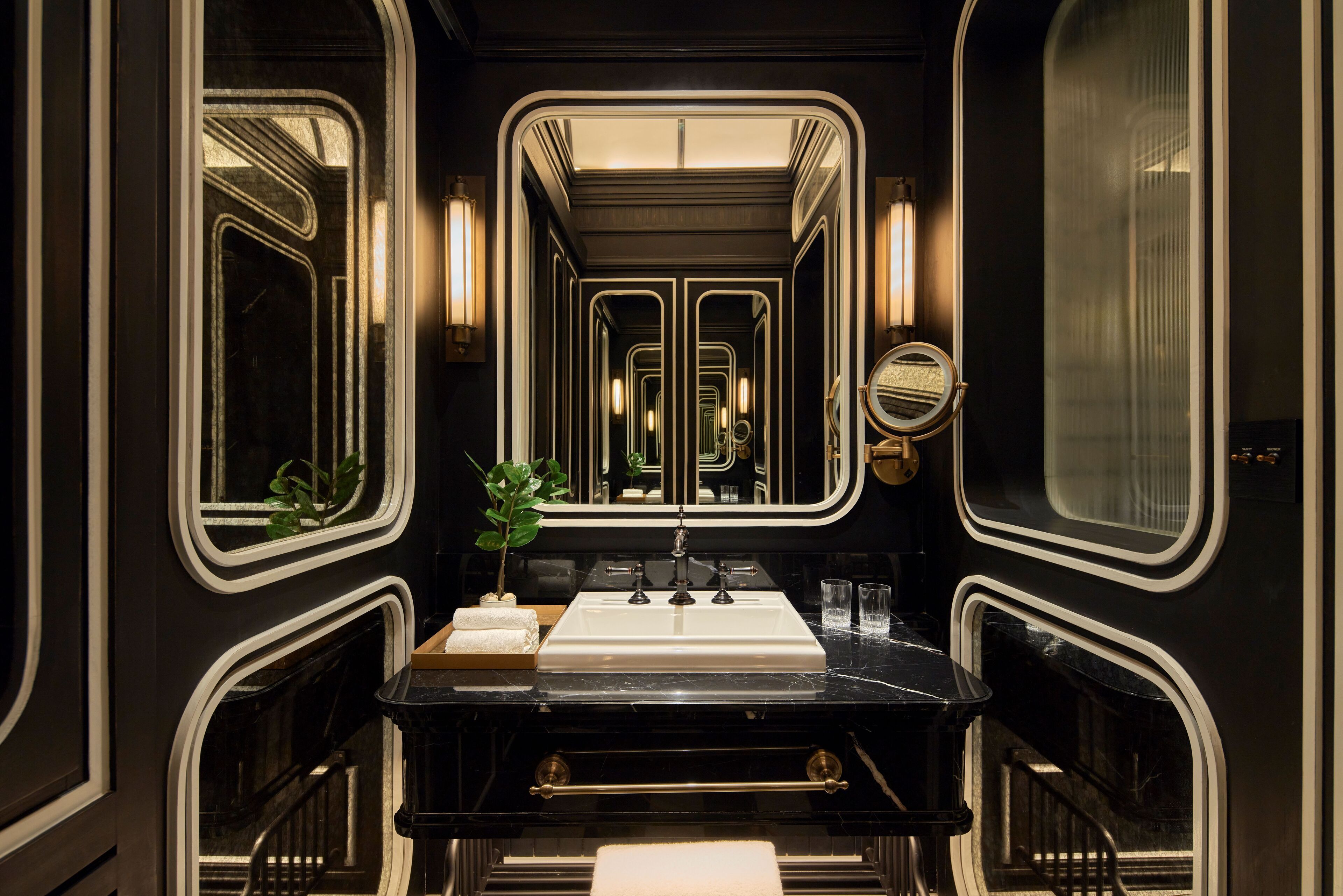 A luxurious bathroom with a black vanity, a large mirror, and a white sink.