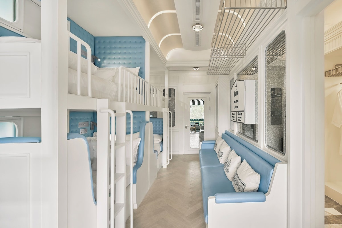 A corridor with bunk beds, a blue bench, and a wardrobe with a hanging robe.