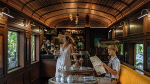 A train dining car with a curved wooden ceiling, a buffet table with tea and pastries, and a yellow cushioned bench. - Intercontinental Khao Yai Resort by IHG (Pak Chong)