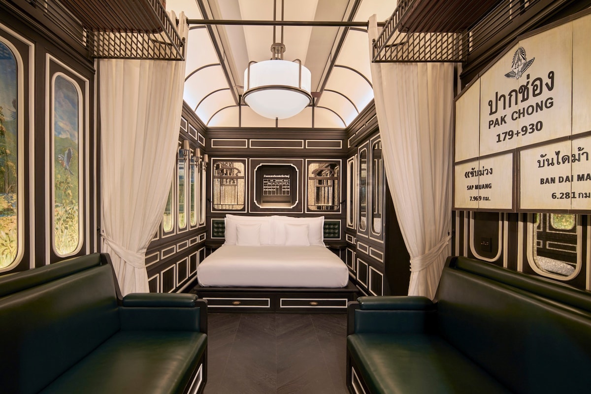 A train carriage bedroom with a bed, curtains, and a mural.