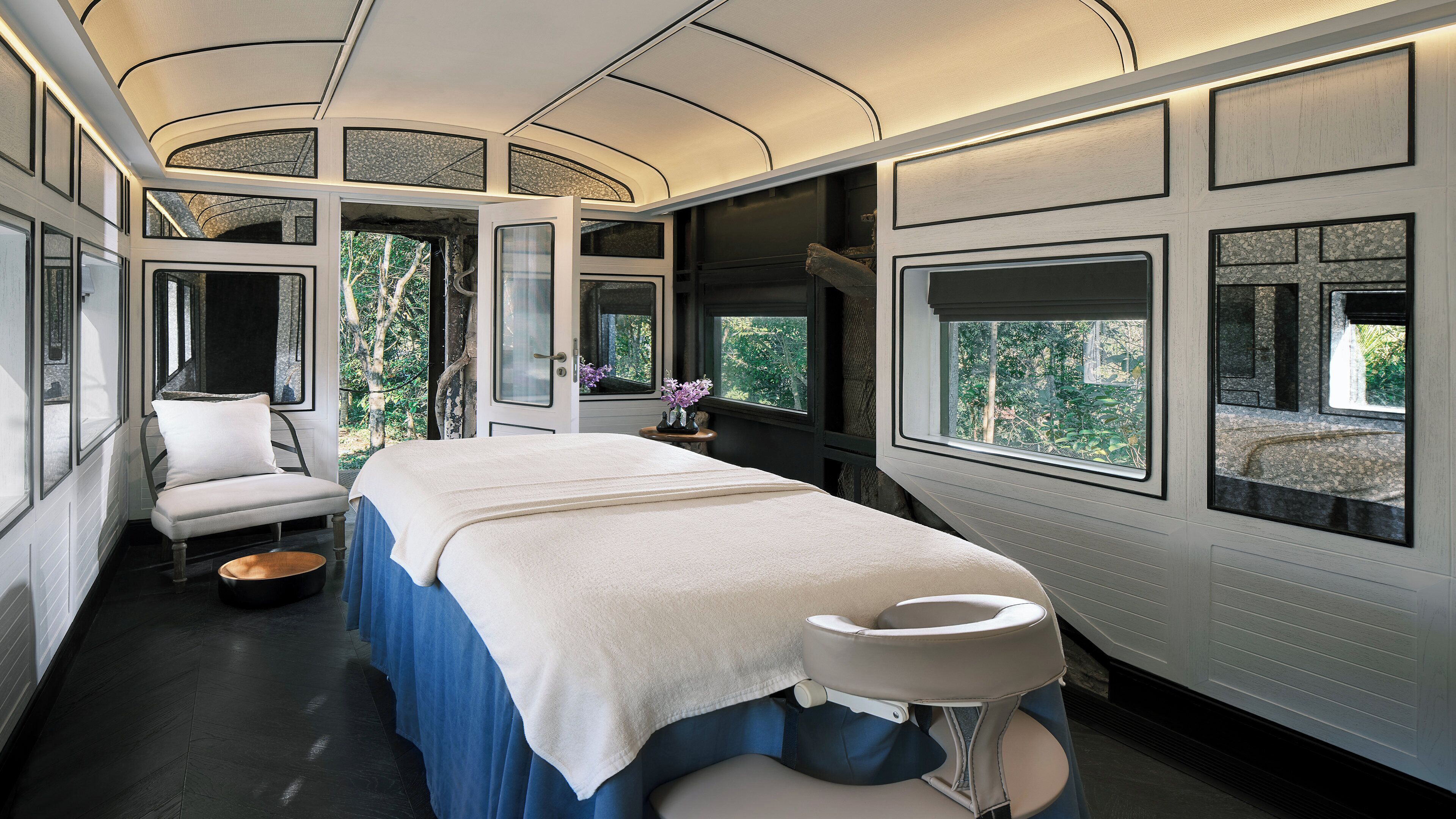 Ein modernes, helles Schlafzimmer mit Bett, Sitzecke und großen Fenstern mit Blick auf Grünflächen.